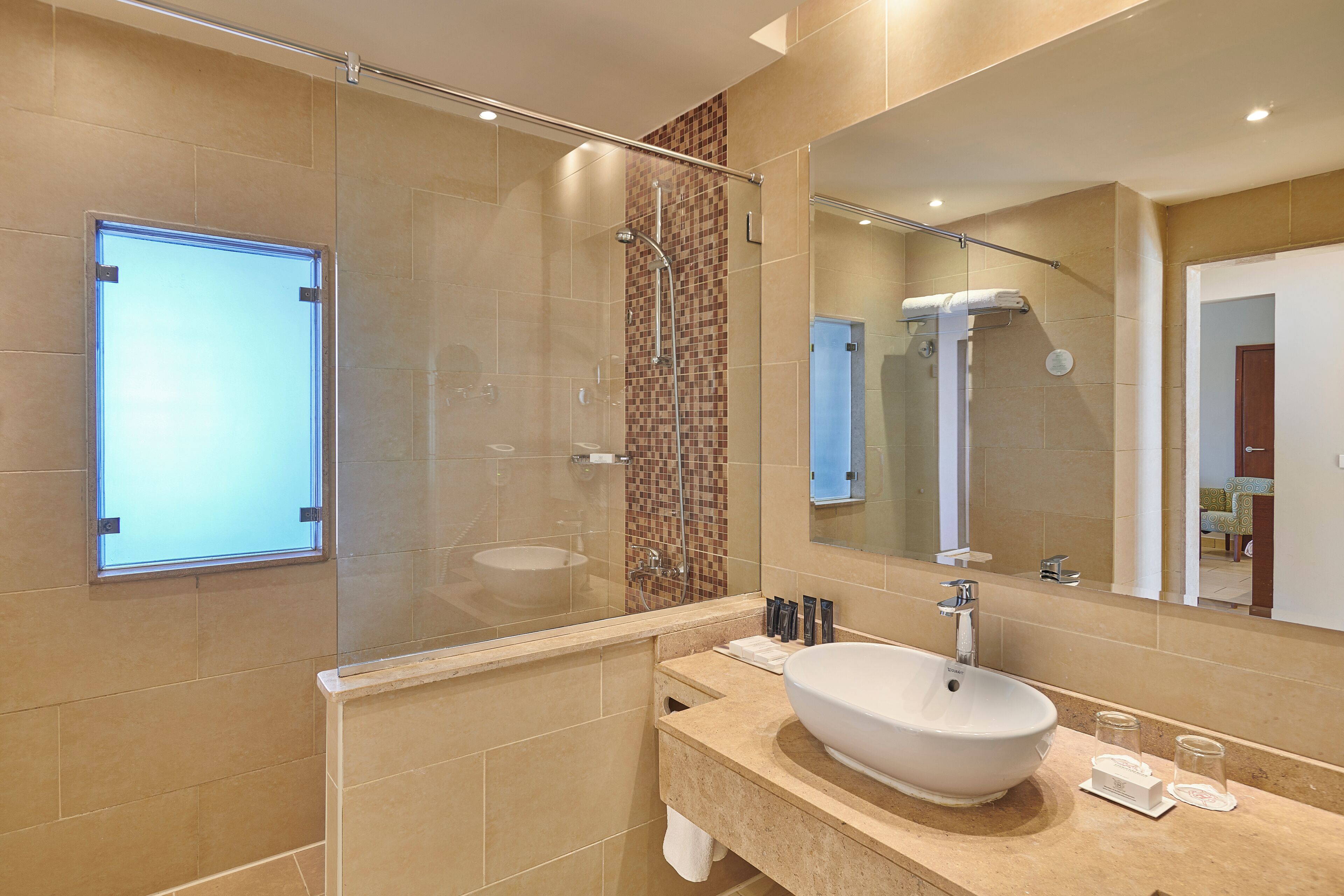 Un baño moderno con ducha de vidrio, un espejo grande y un lavamanos con azulejos color beige.