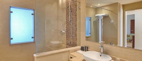 A modern bathroom with a glass-enclosed shower, a large mirror, and a beige-tiled sink.