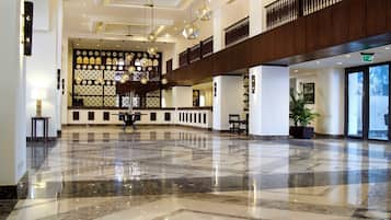 Un lobby espacioso con suelo de mármol pulido, una recepción de madera y una pared decorativa con diseños intrincados.