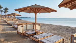 Un hotel frente a la playa con tumbonas y sombrillas de madera, una playa de arena y un mar tranquilo.