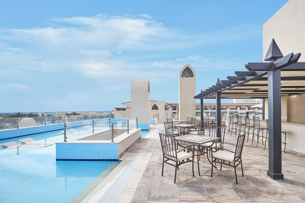 Zona d'una piscina al terrat amb vista clara al mar, mobiliari exterior i un element arquitectònic característic.