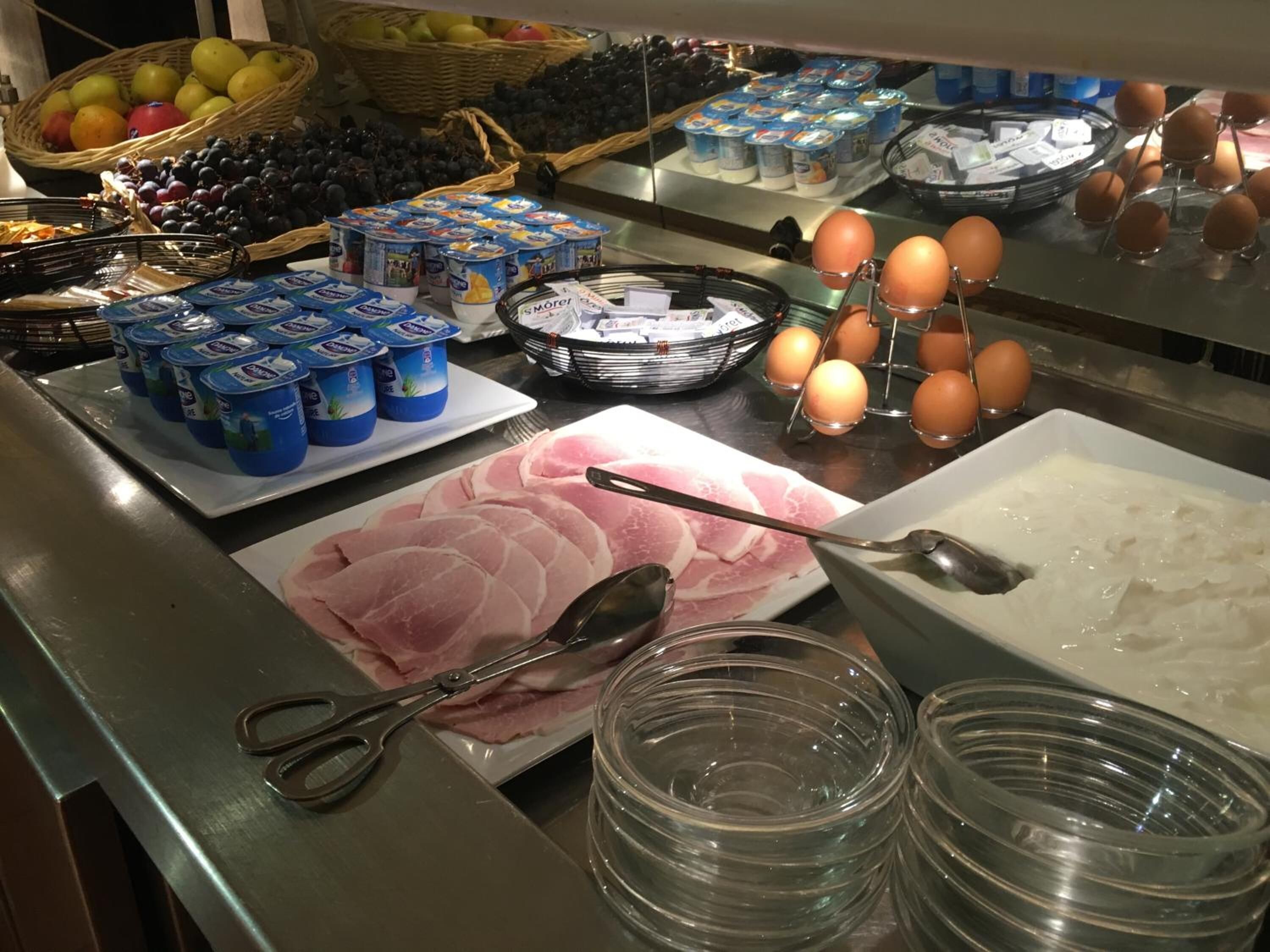 Een buffet met diverse etenswaren, waaronder yoghurt, eieren en vleesschotel.