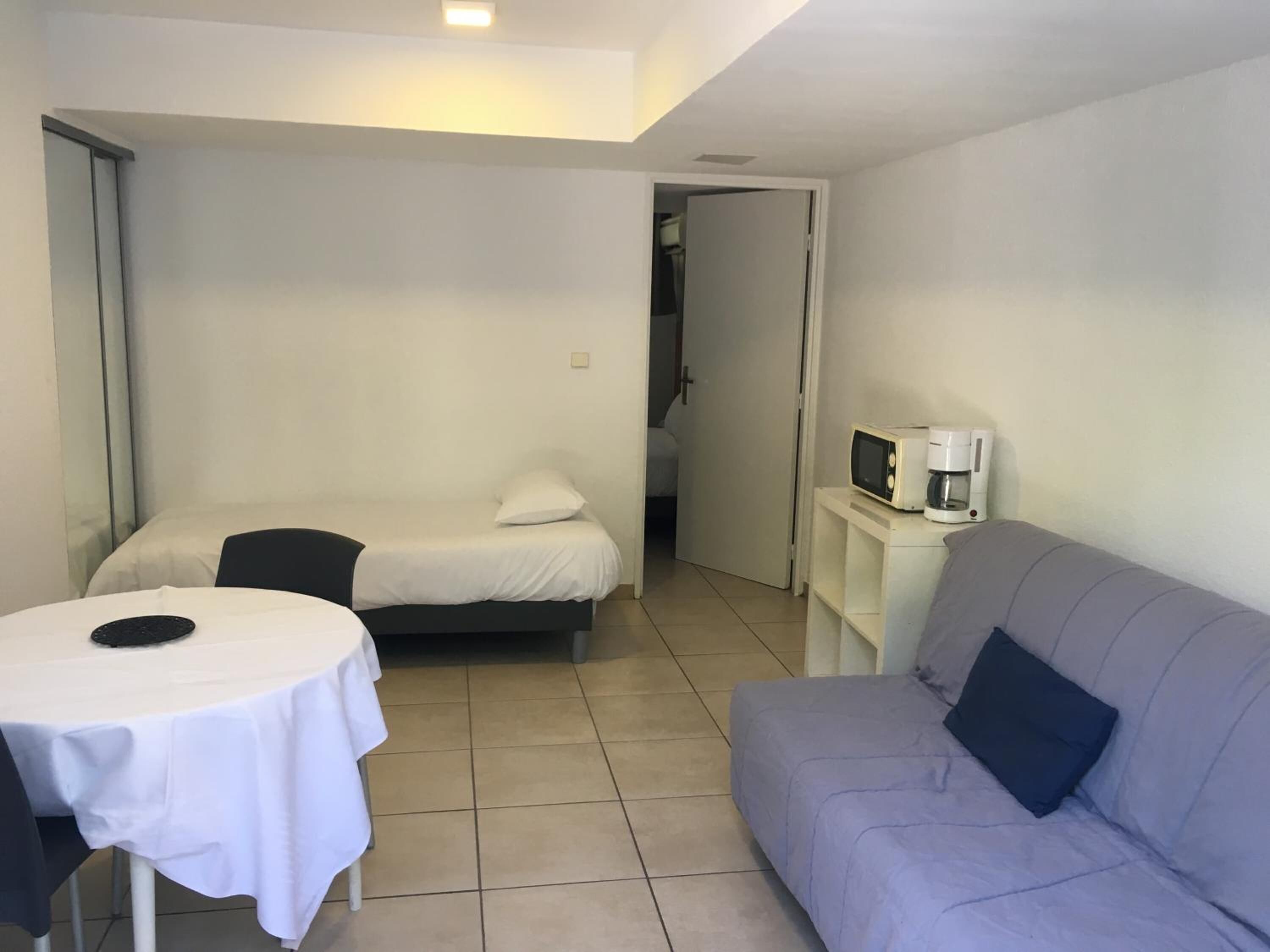 Una habitación pequeña y bien iluminada con una cama, un sofá, una mesa con un plato y un microondas sobre una mesita.