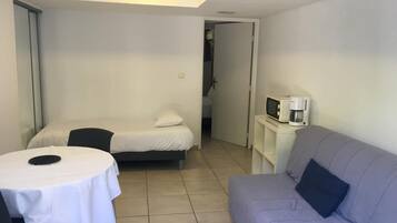 Una habitación pequeña y bien iluminada con una cama, un sofá, una mesa con un plato y un microondas sobre una mesita.