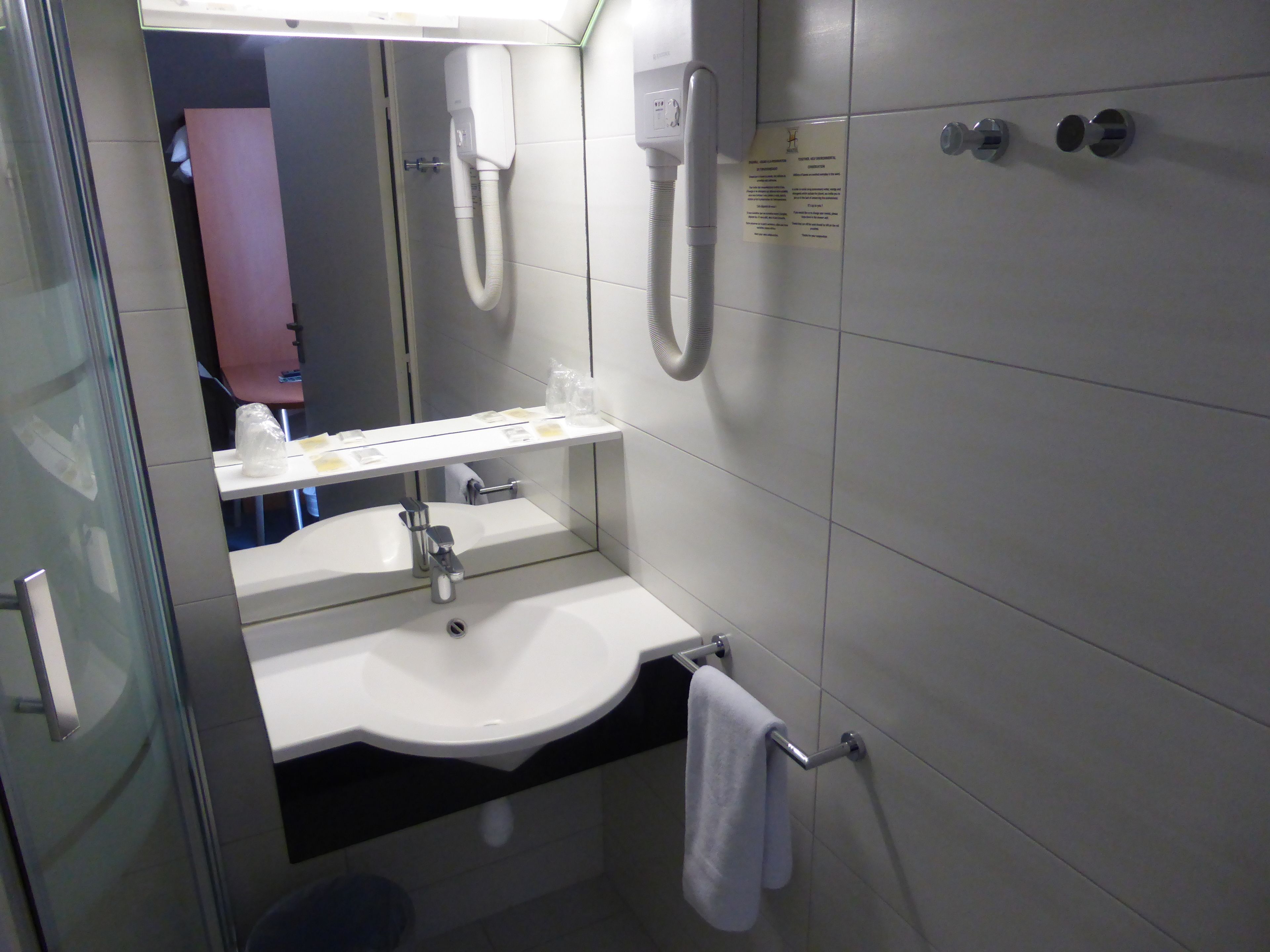 Un baño moderno con un lavabo blanco, espejo y toallero.