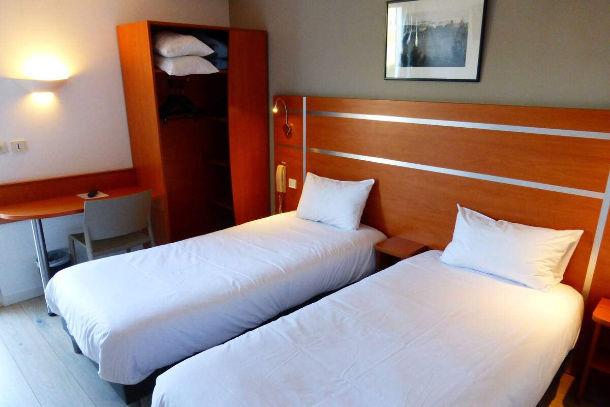 A hotel room with two single beds, a desk, a chair, and a wardrobe.