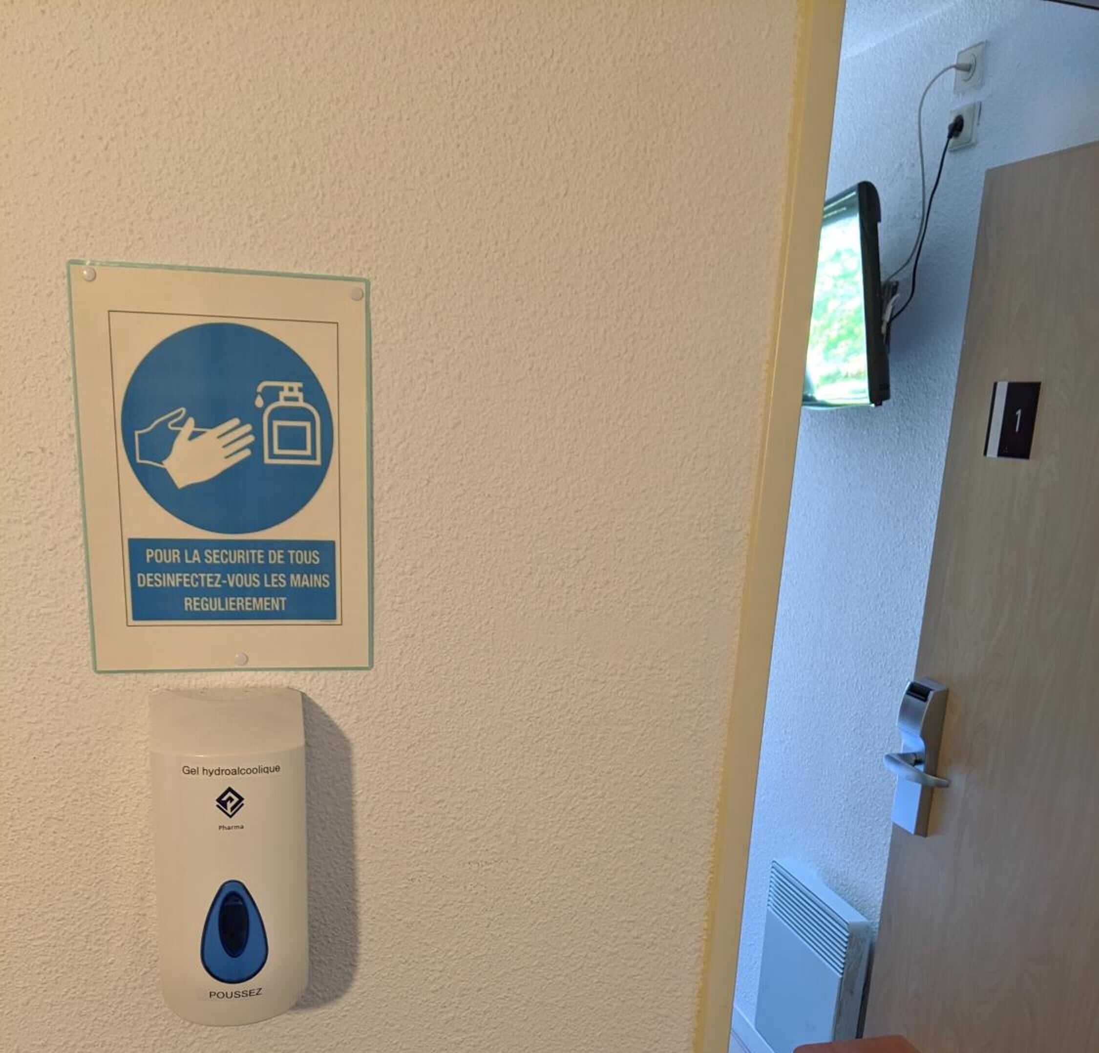 A hand sanitizer dispenser mounted on a wall with a sign above it.