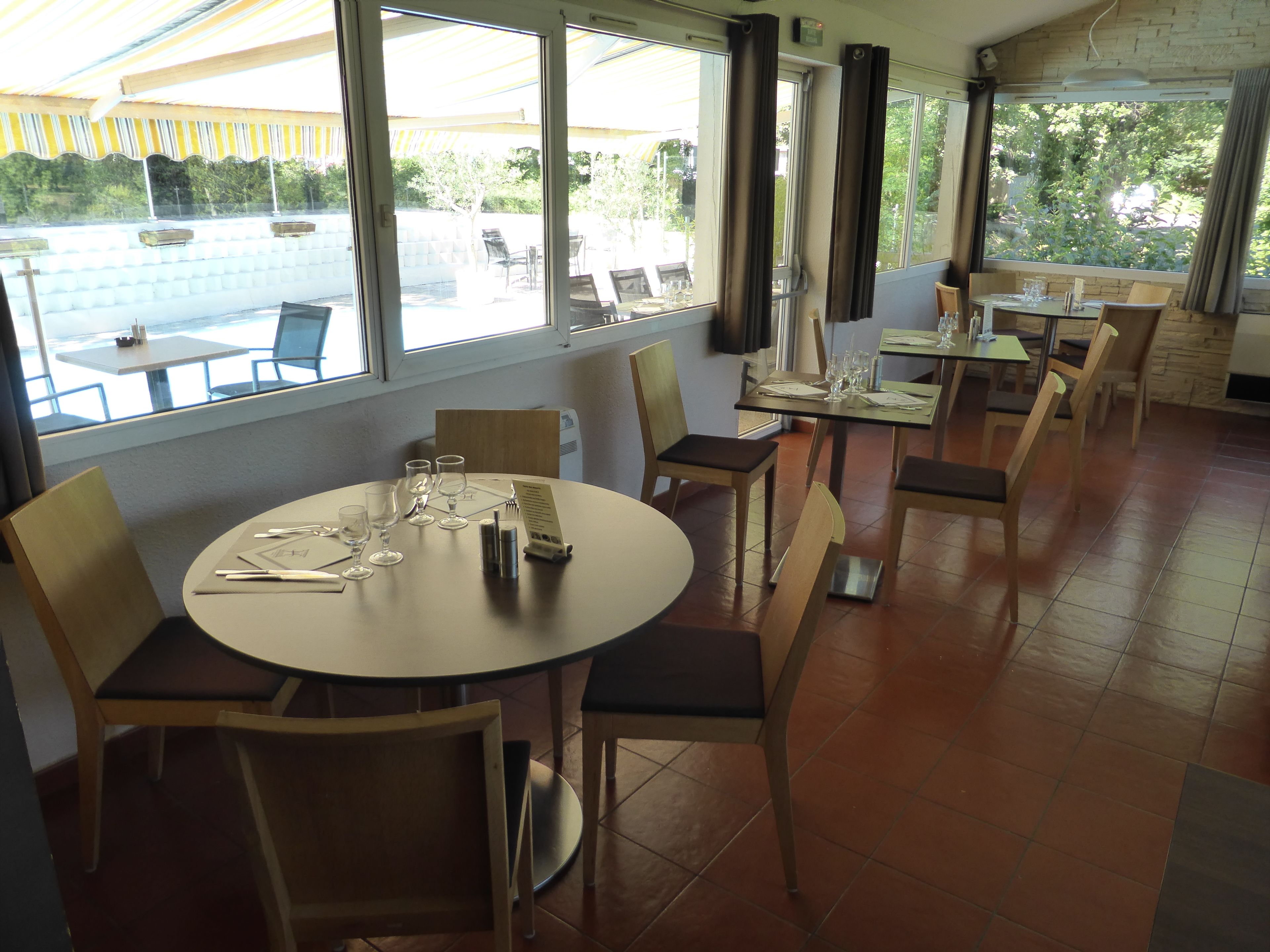 Un restaurante con mesas y sillas redondas, ventanas amplias y vista al área de mesas al aire libre.