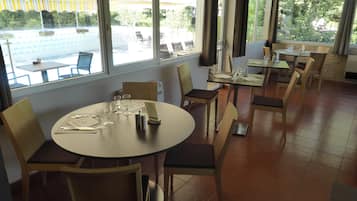 Un restaurante con mesas y sillas redondas, ventanas amplias y vista al área de mesas al aire libre.