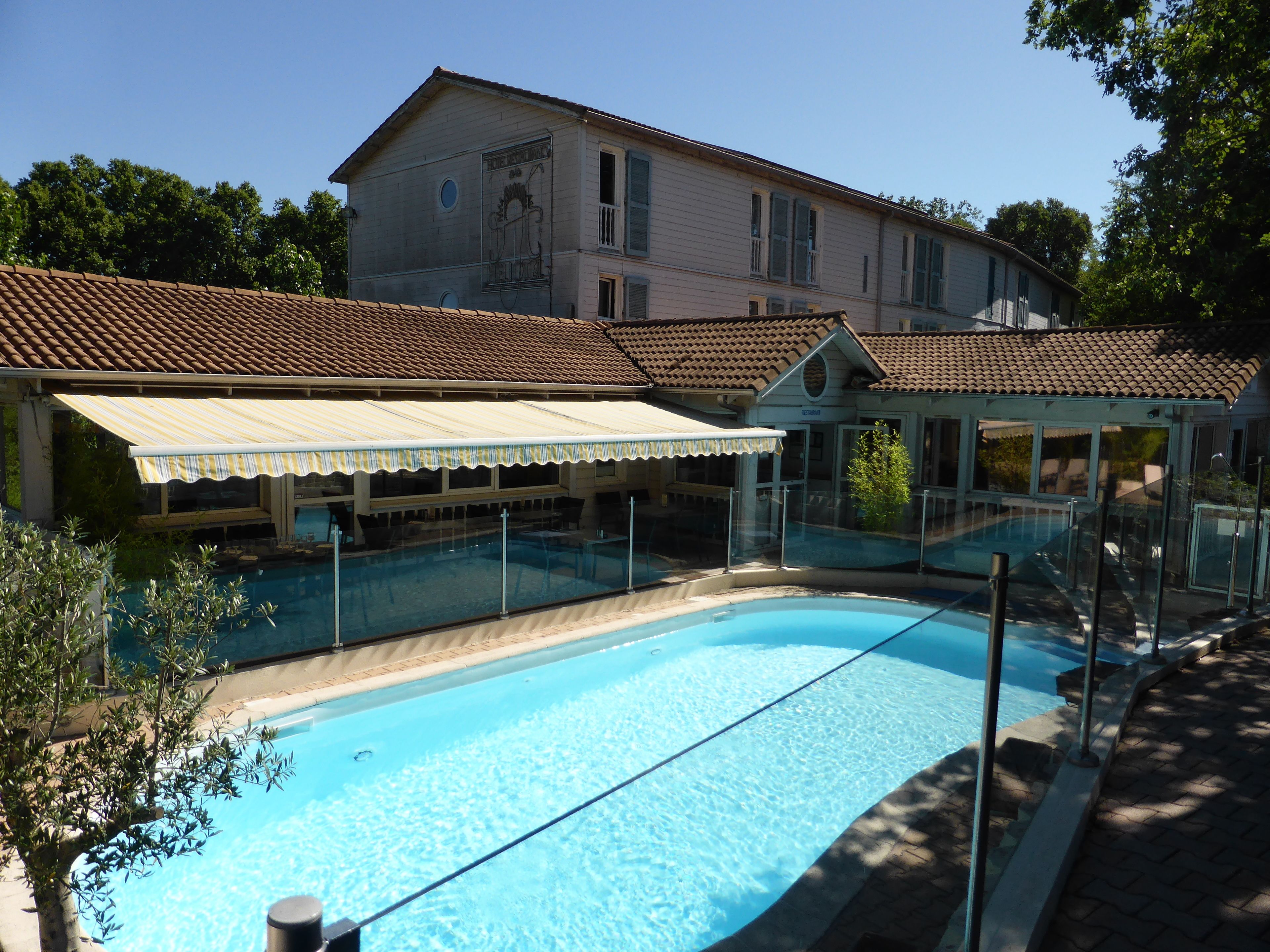 Una piscina con una zona techada y un edificio al fondo.