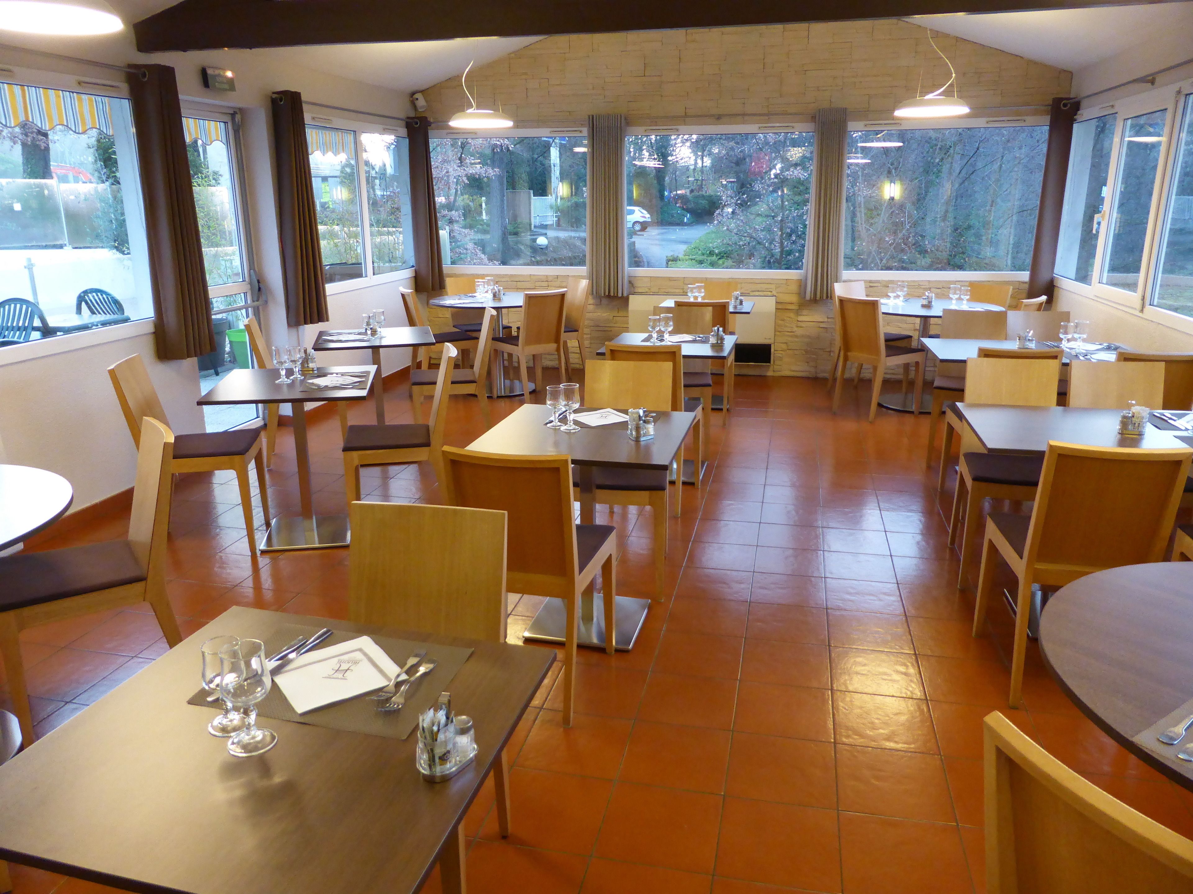 A restaurant with multiple tables and chairs, large windows with curtains, and a tiled floor.