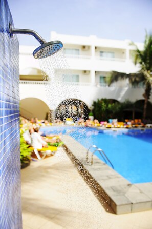 Zona de piscina con fuente, pared de azulejos y un edificio al fondo.