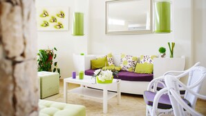 Una sala de estar moderna con un sofá blanco, cojines verdes, una mesa de centro blanca y una silla de mimbre.