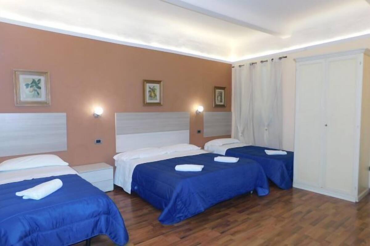 A hotel room with three beds, a wardrobe, and wall-mounted lights.
