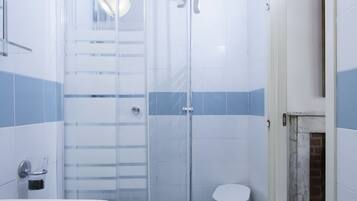 Un baño con ducha de vidrio, una bañera blanca y un taburete blanco pequeño.