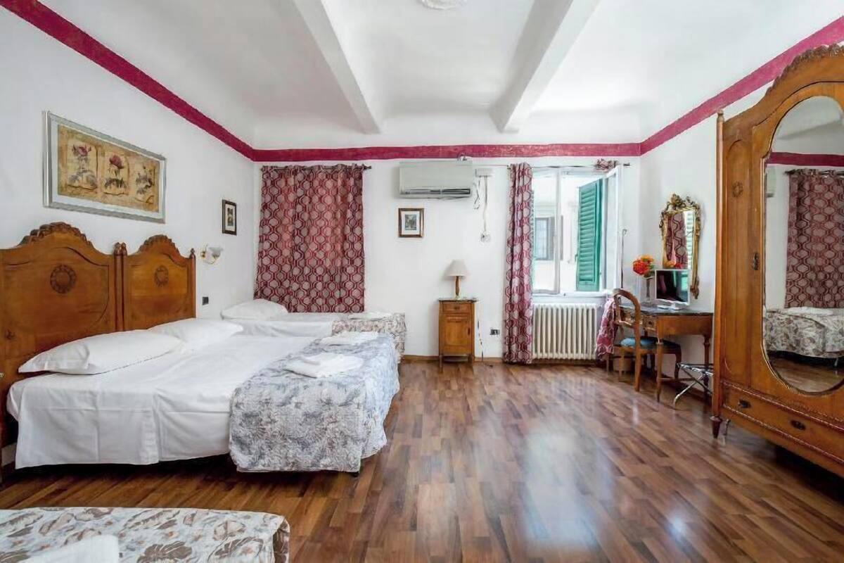 A room with two beds, a wooden desk, a chair, a mirror, and a radiator.