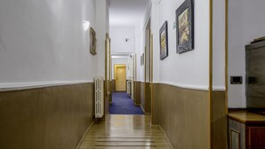 A hallway with a blue carpet, wooden floor, white walls, and framed pictures on the walls. - Piccolo Hotel (Florence)