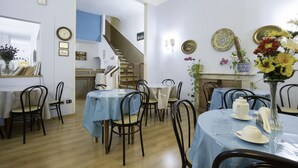 A dining area with multiple tables and chairs, a staircase, and decorative wall plates. - Piccolo Hotel (Florence)