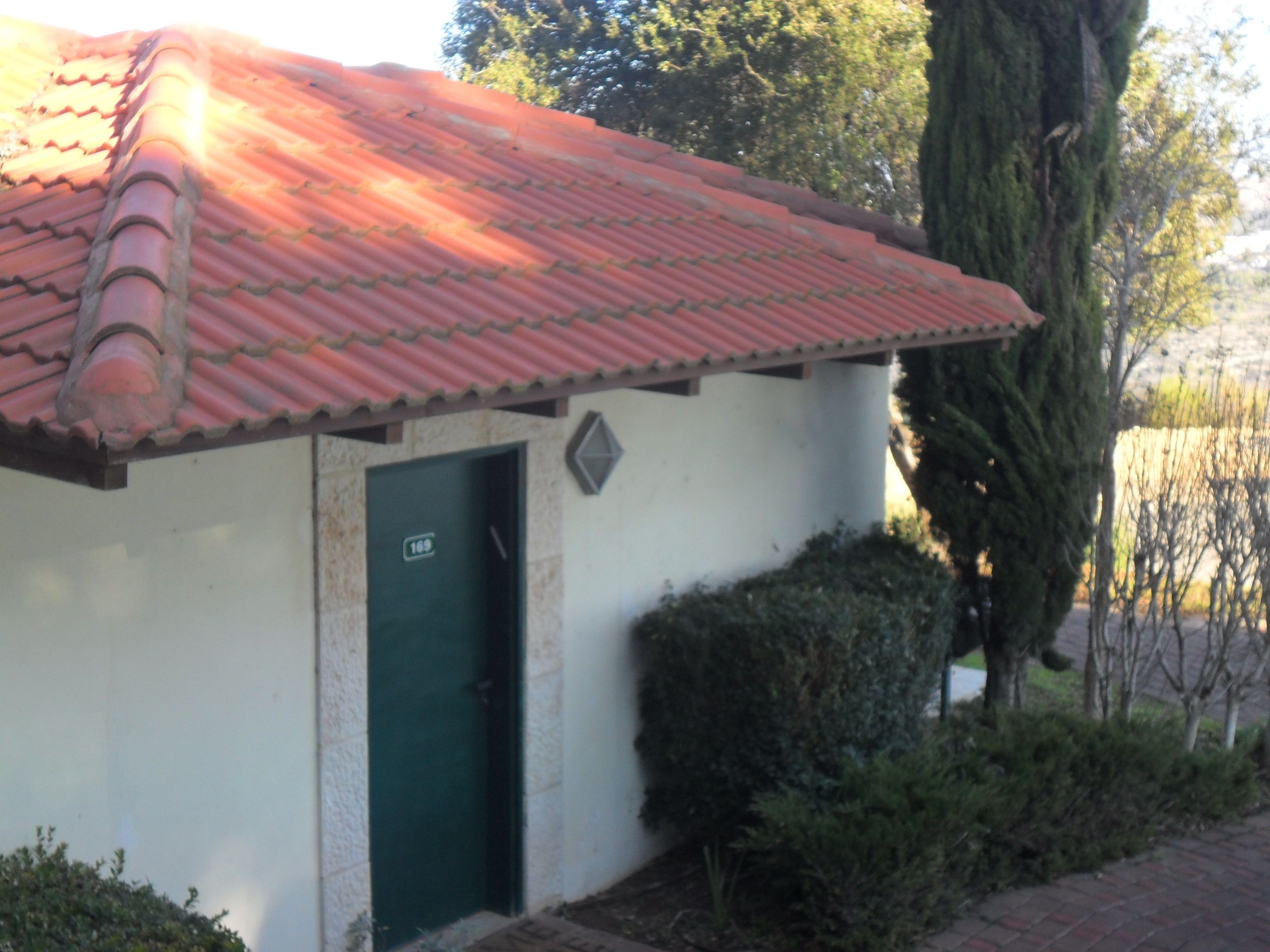 Un edifici amb teules vermelles al sostre, una porta verda i el número 169 a la porta.