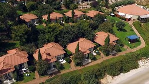 Vista aérea de una zona residencial con casas de tejas rojas, rodeada de vegetación y una playa.