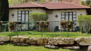 A two-story house with a tiled roof, a stone wall in front, and a green fence.