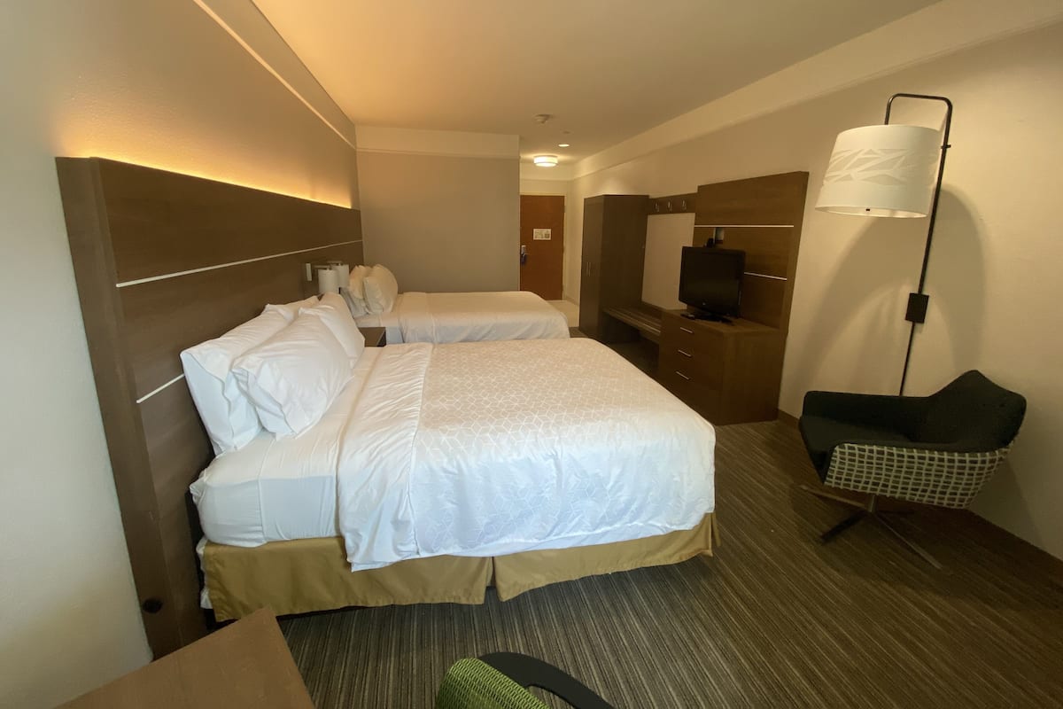 A hotel room with two beds, a desk, a chair, a television, and a wardrobe.