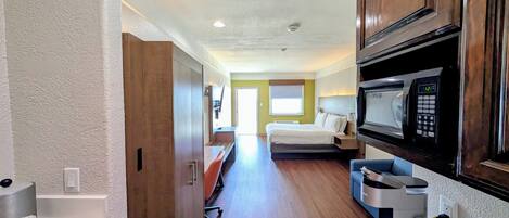 Habitación de hotel pequeña con kitchenette, una cama y vista al pasillo.