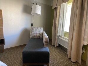 Una habitación pequeña y ordenada con una cama individual, una lámpara de noche, un radiador y una ventana con cortinas.