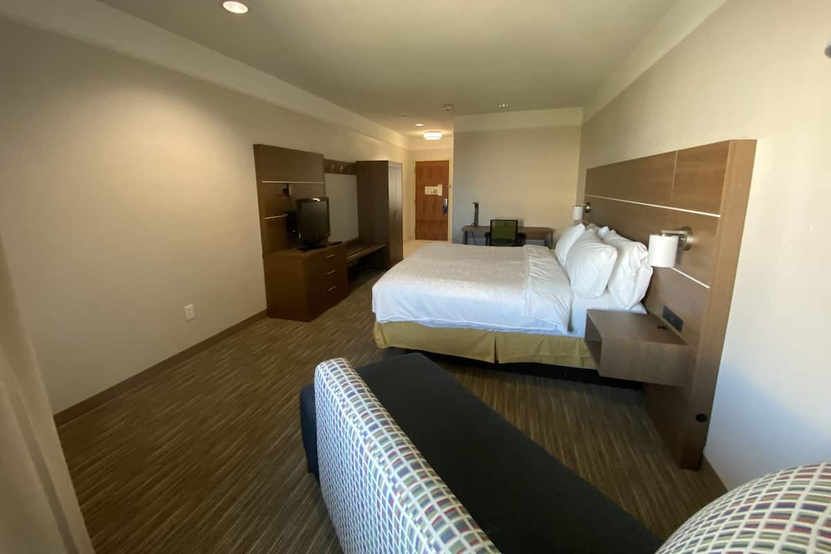 A hotel room with a large bed, a desk with a chair, a television, and a wardrobe.