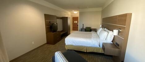 A hotel room with a large bed, a desk with a chair, a television, and a wardrobe.