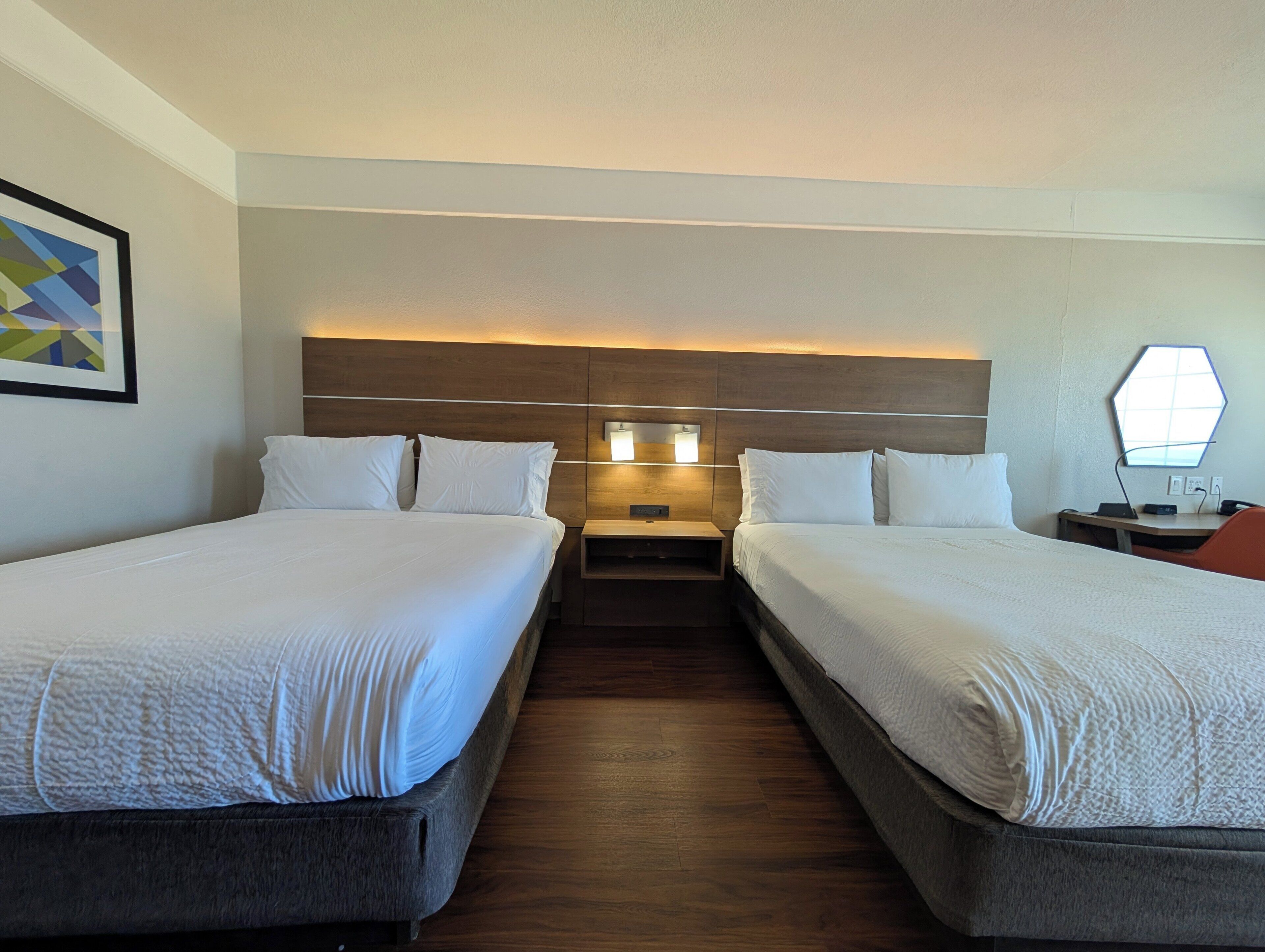 A hotel room with two beds, a nightstand, a desk, and a wall-mounted lamp.