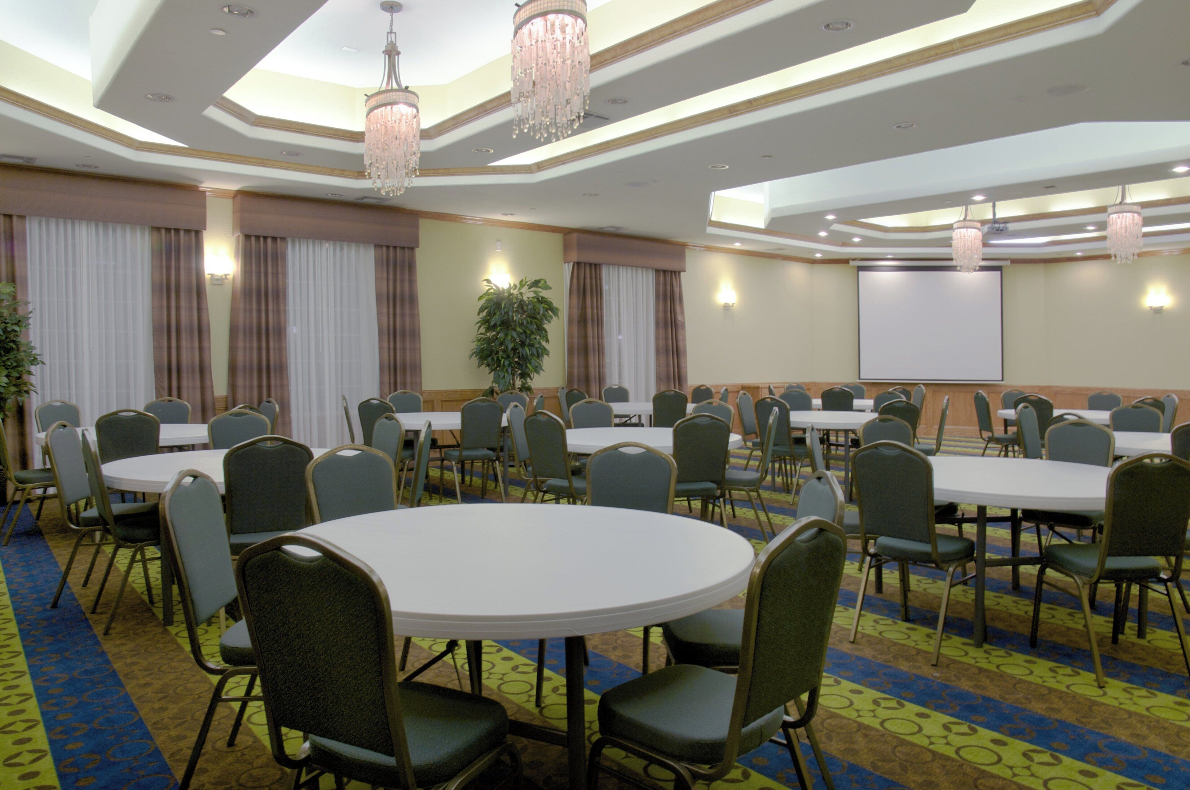 Un salón de conferencias con mesas redondas, sillas, una pantalla de proyector y candelabros.