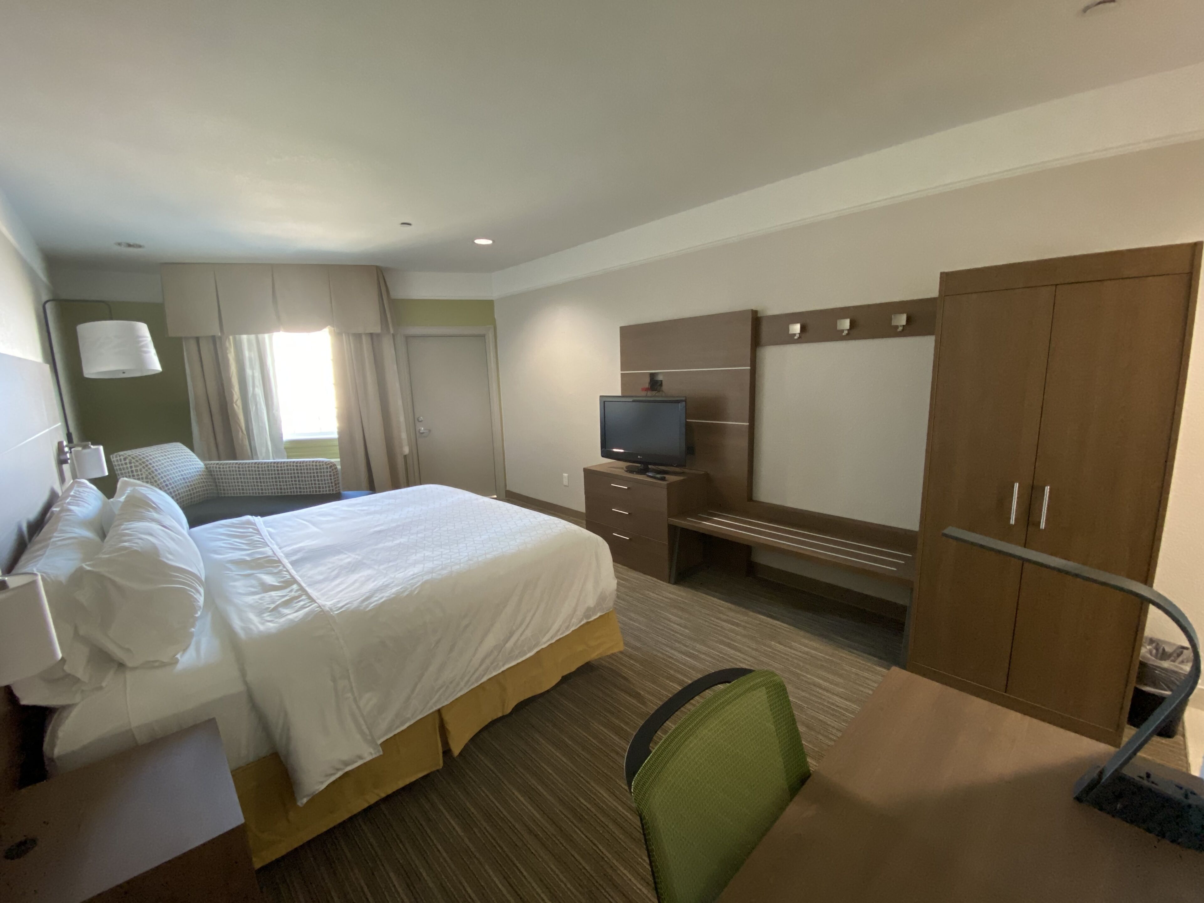 Una habitación de hotel con cama, escritorio, televisor y armario.