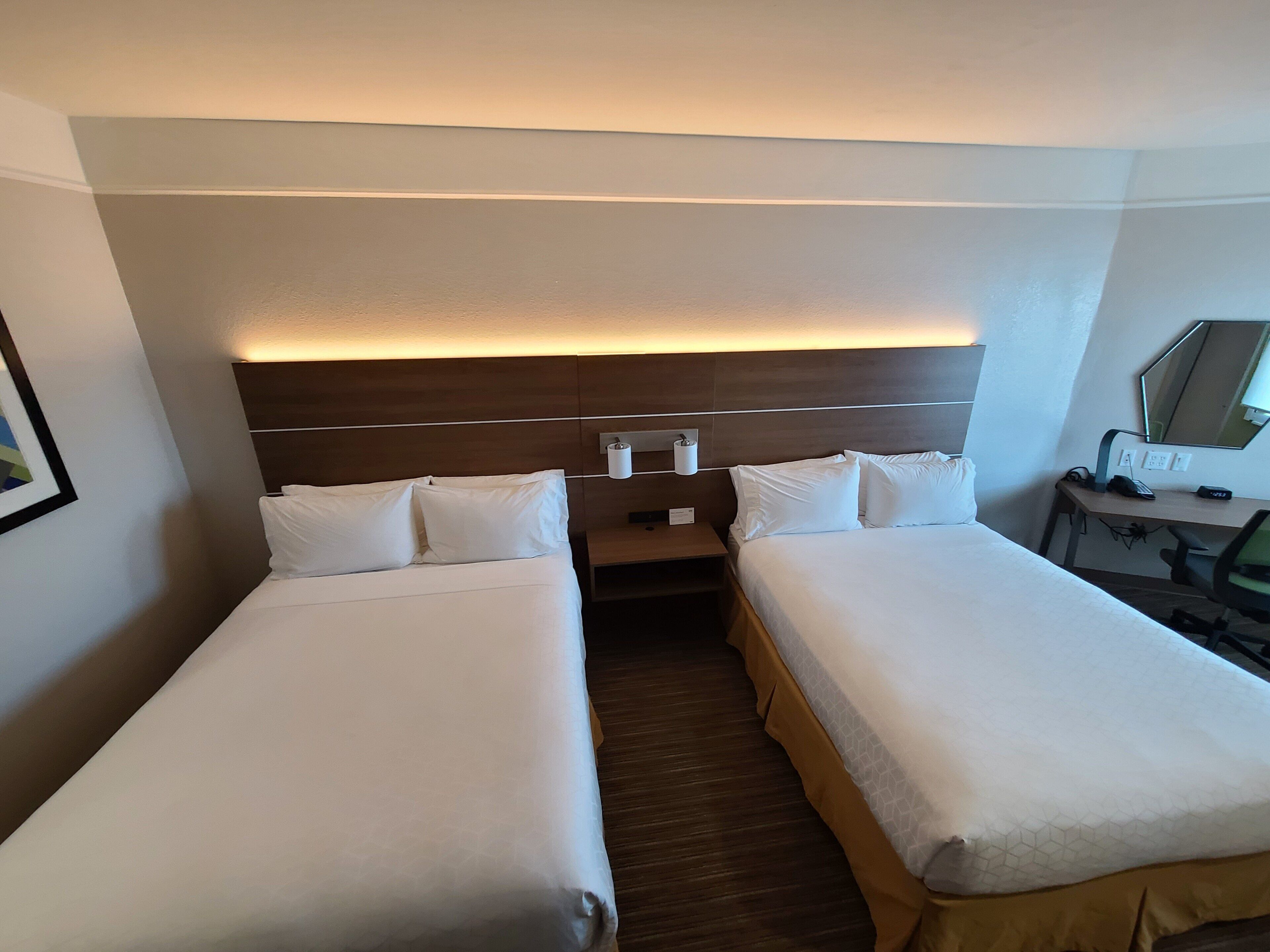 Ett hotellrum med två sängar, ett skrivbord, en stol, en spegel och en väggmonterad lampa.