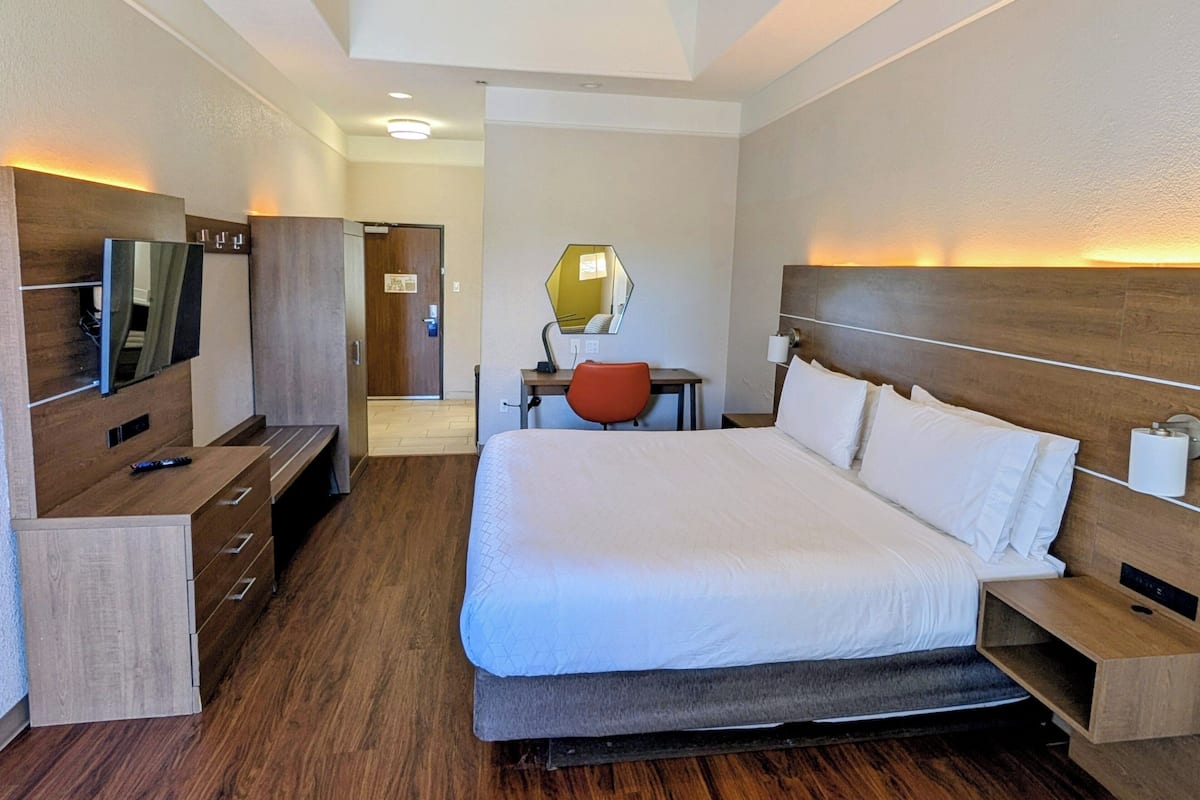 A hotel room with a large bed, a desk with a chair, a television, and a mirror.