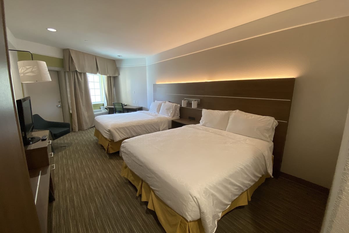 A hotel room with two beds, a desk with a computer, a TV, and a lamp.