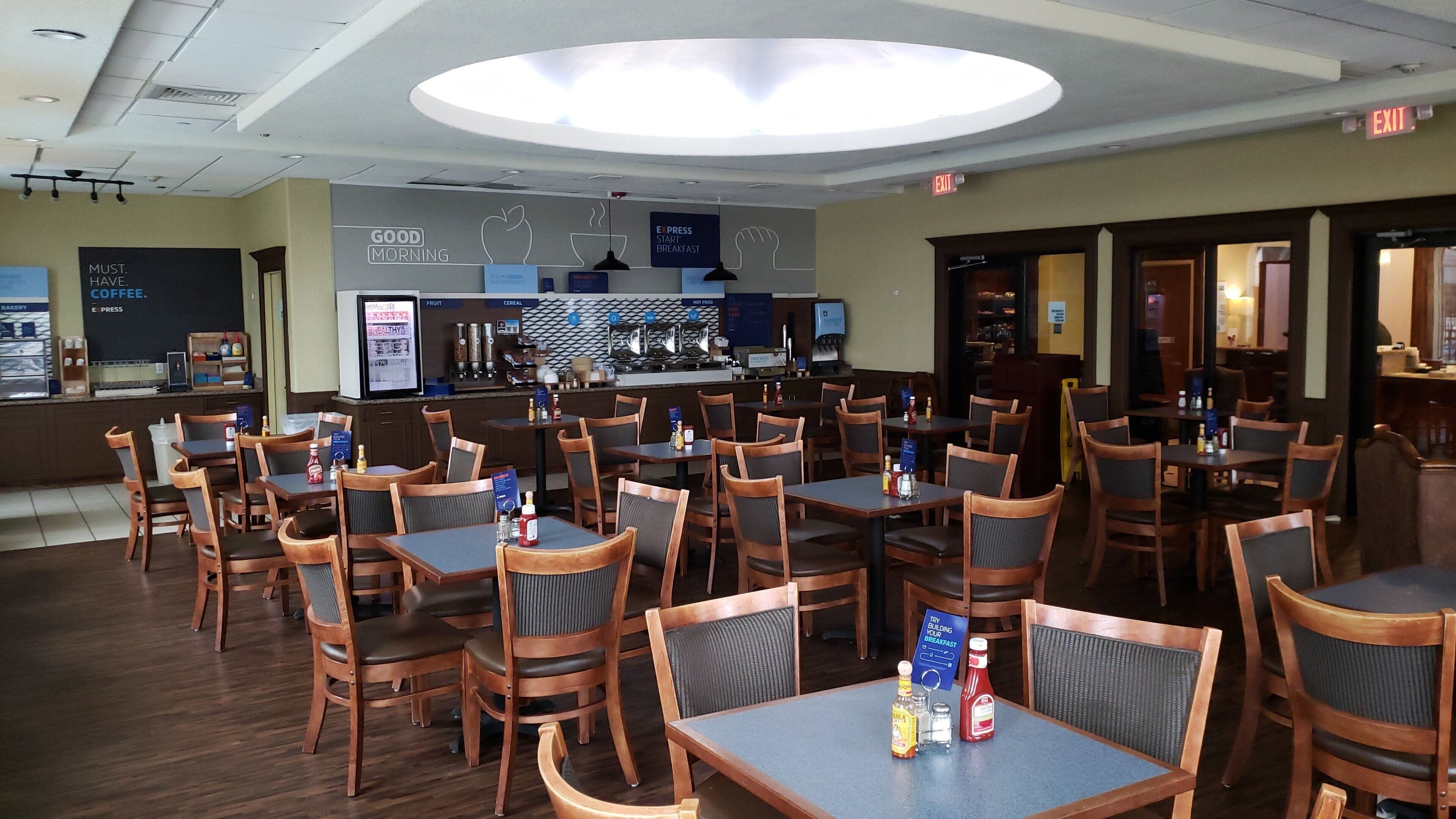 A restaurant with multiple tables and chairs, a bar area, and signs indicating breakfast options.