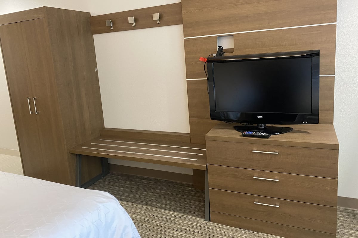 A hotel room with a bed, a wooden wardrobe, a television, and a desk with drawers.