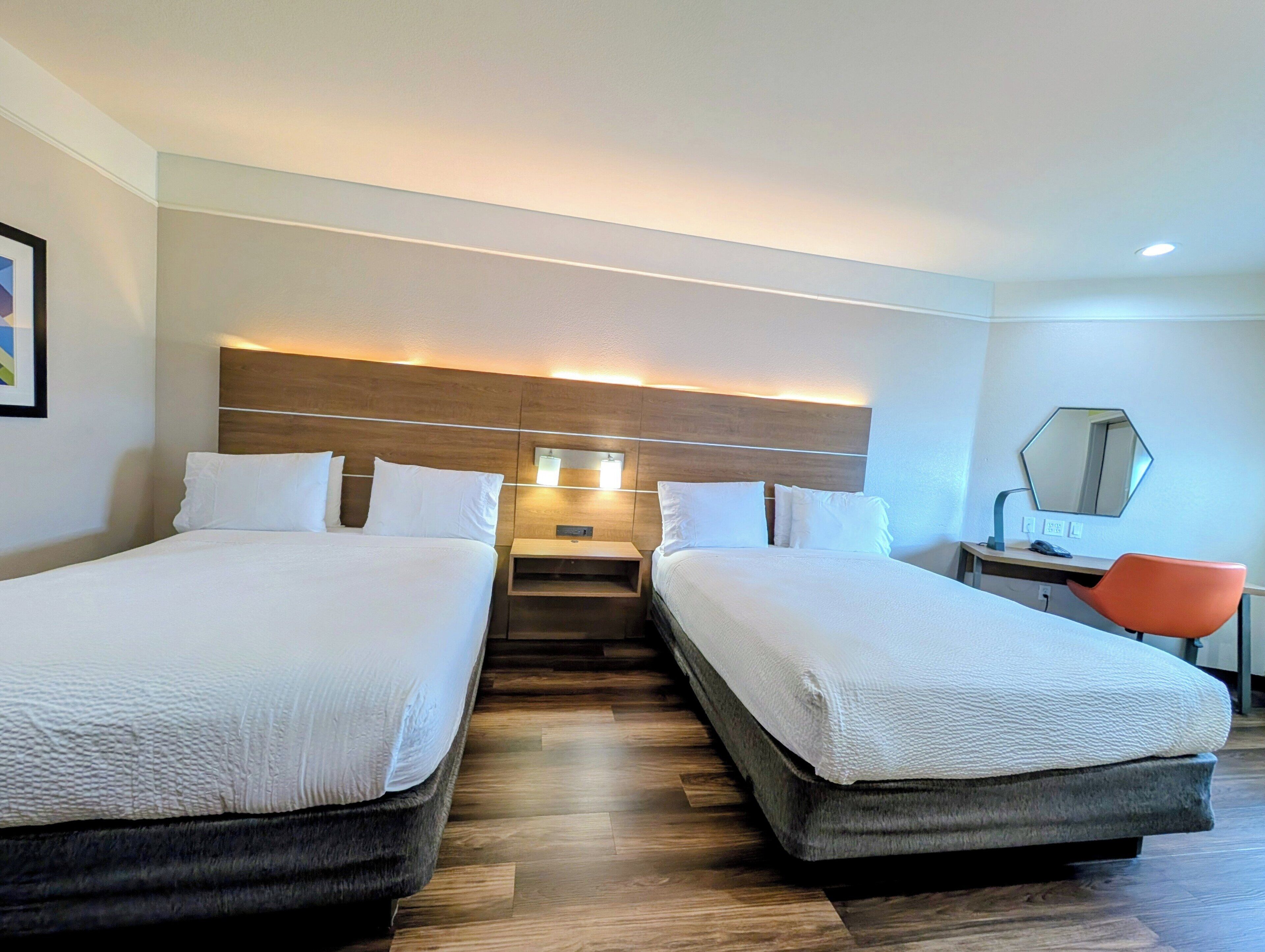 A hotel room with two beds, a desk, a chair, a mirror, and a staircase.