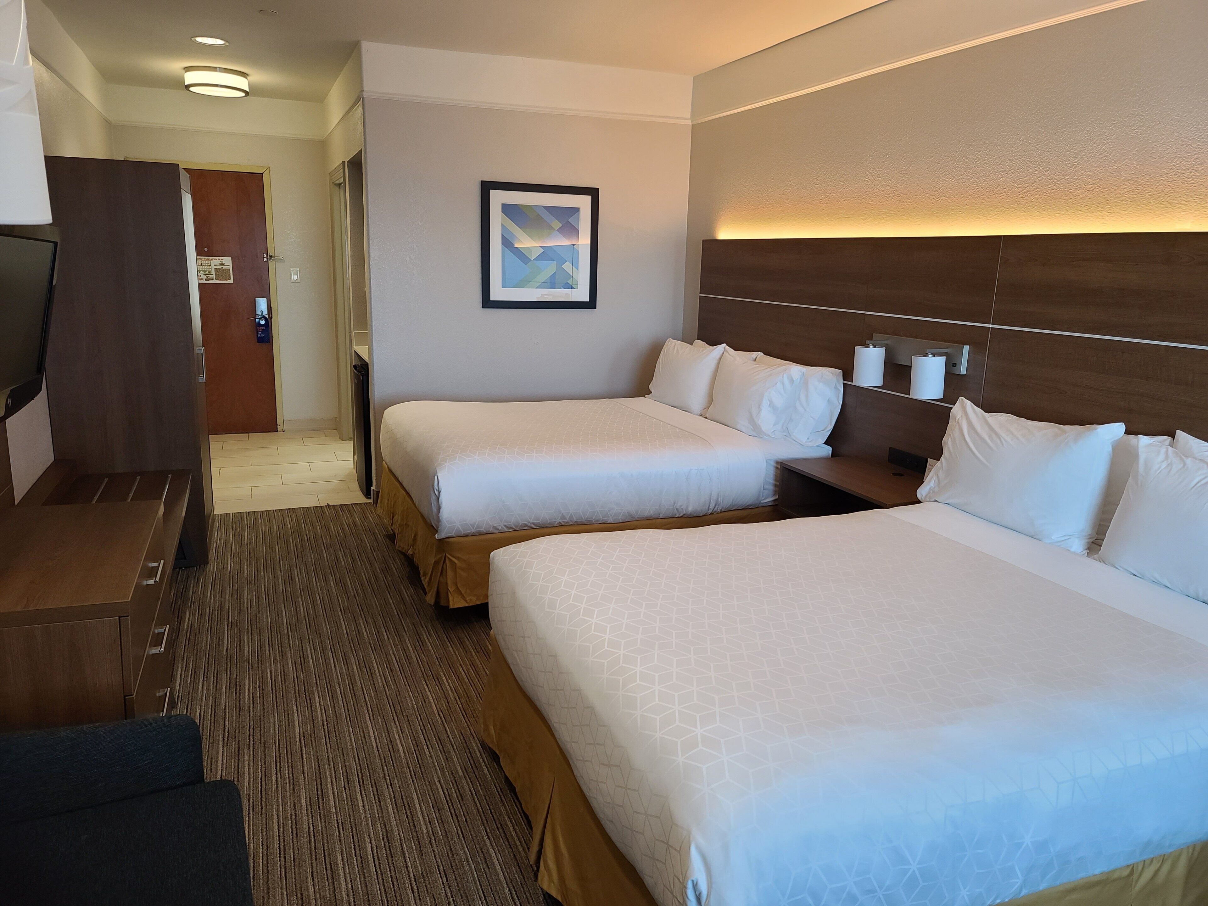 A hotel room with two beds, a desk, a chair, a framed picture on the wall, and a wooden headboard.