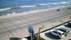 Una carretera costera con vista a la playa, coches estacionados y un letrero de hotel.