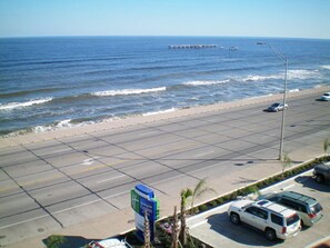Una carretera costera con vista a la playa, coches estacionados y un letrero de hotel.