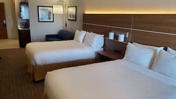 A hotel room with two beds, a desk, a chair, a coffee machine, and framed artwork on the wall.