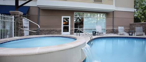 Una piscina con hidromasaje, un área techada con una escalera y un edificio con puerta y ventanas.
