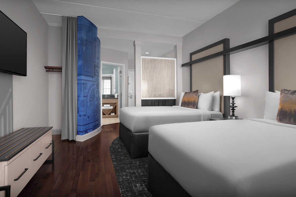 Une chambre d’hôtel avec deux lits, une télévision, un bureau et une salle de bain visible à travers une porte ouverte.