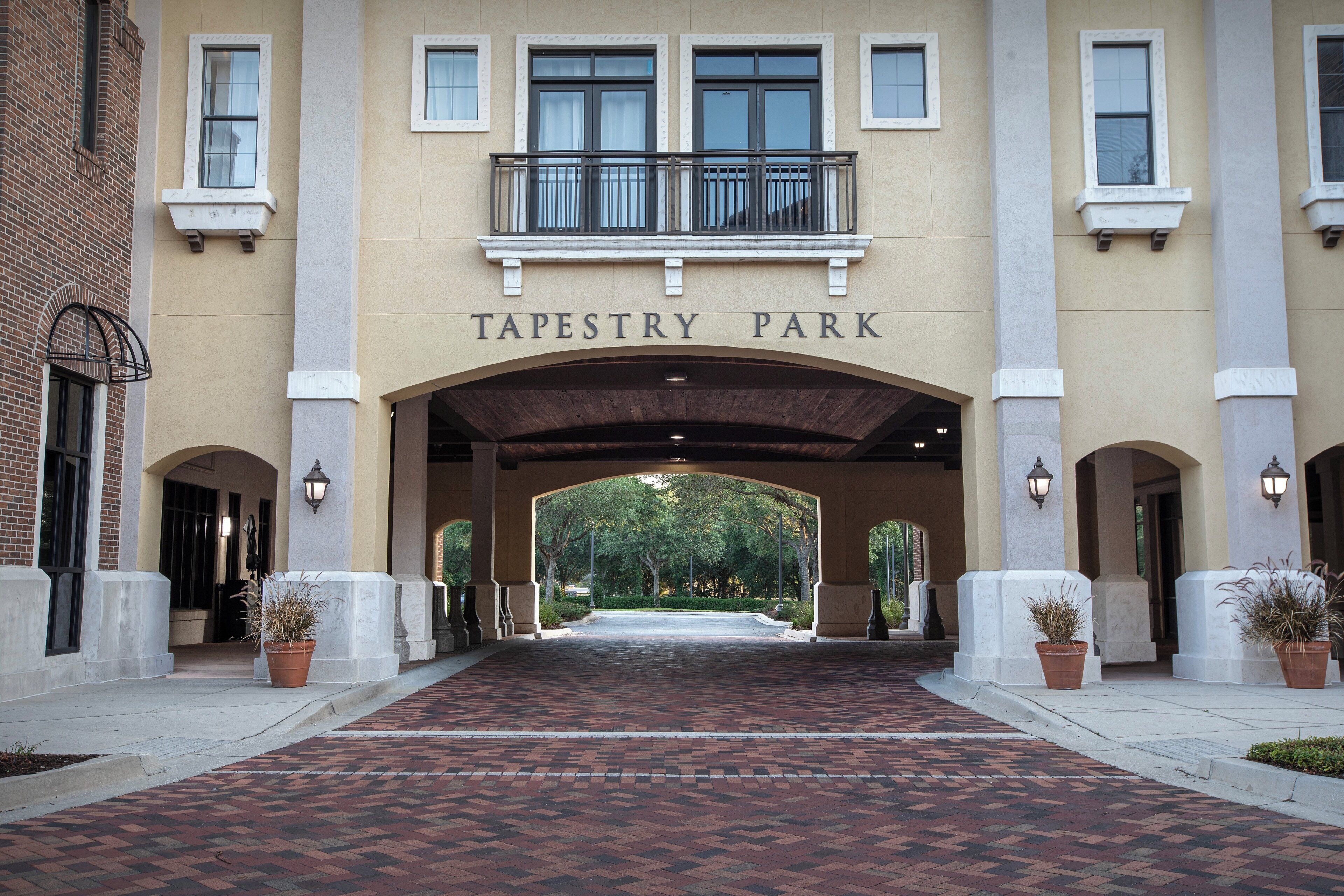 Una entrada de edificio con un letrero que dice 'TAPESTRY PARK' y un camino de ladrillo que conduce a la entrada.