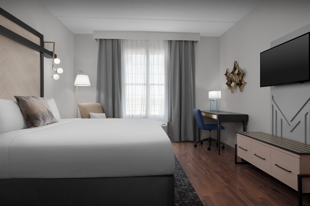 Une chambre d’hôtel moderne équipée d’un grand lit, d’un bureau, d’une chaise, d’une télévision et d’une lampe de bureau.