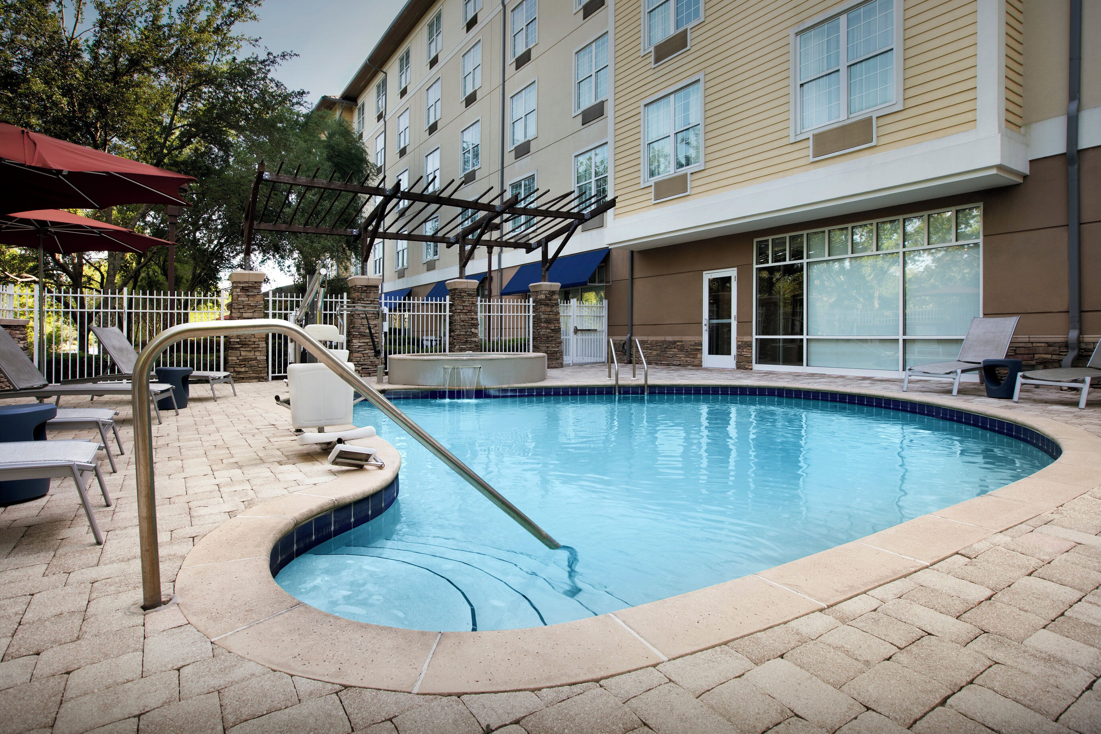 A swimming pool with a stone border, lounge chairs, and umbrellas.