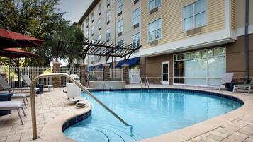 A swimming pool with a stone border, lounge chairs, and umbrellas.