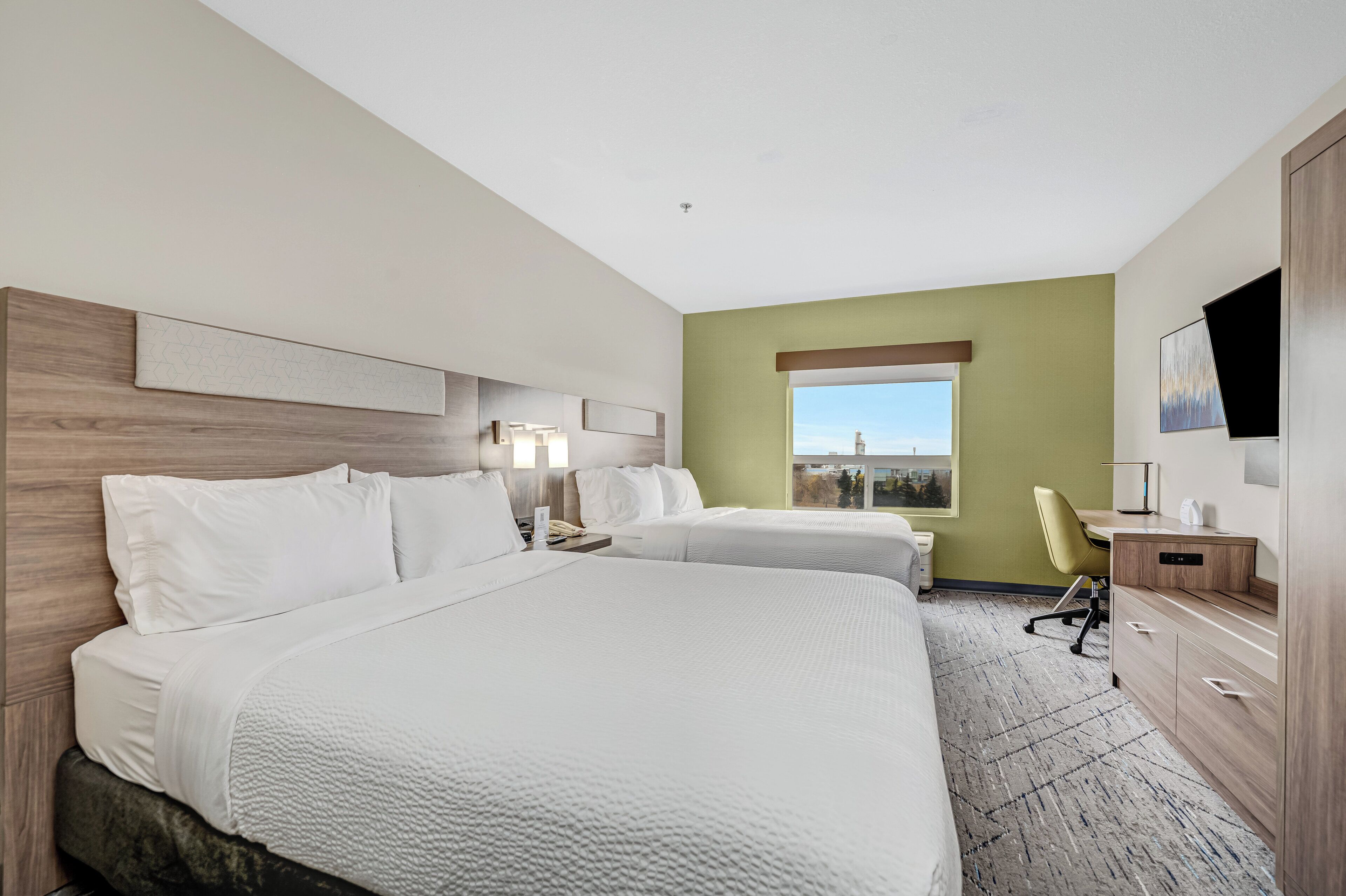 A hotel room with two beds, a desk, a chair, a TV, and a window with a view.